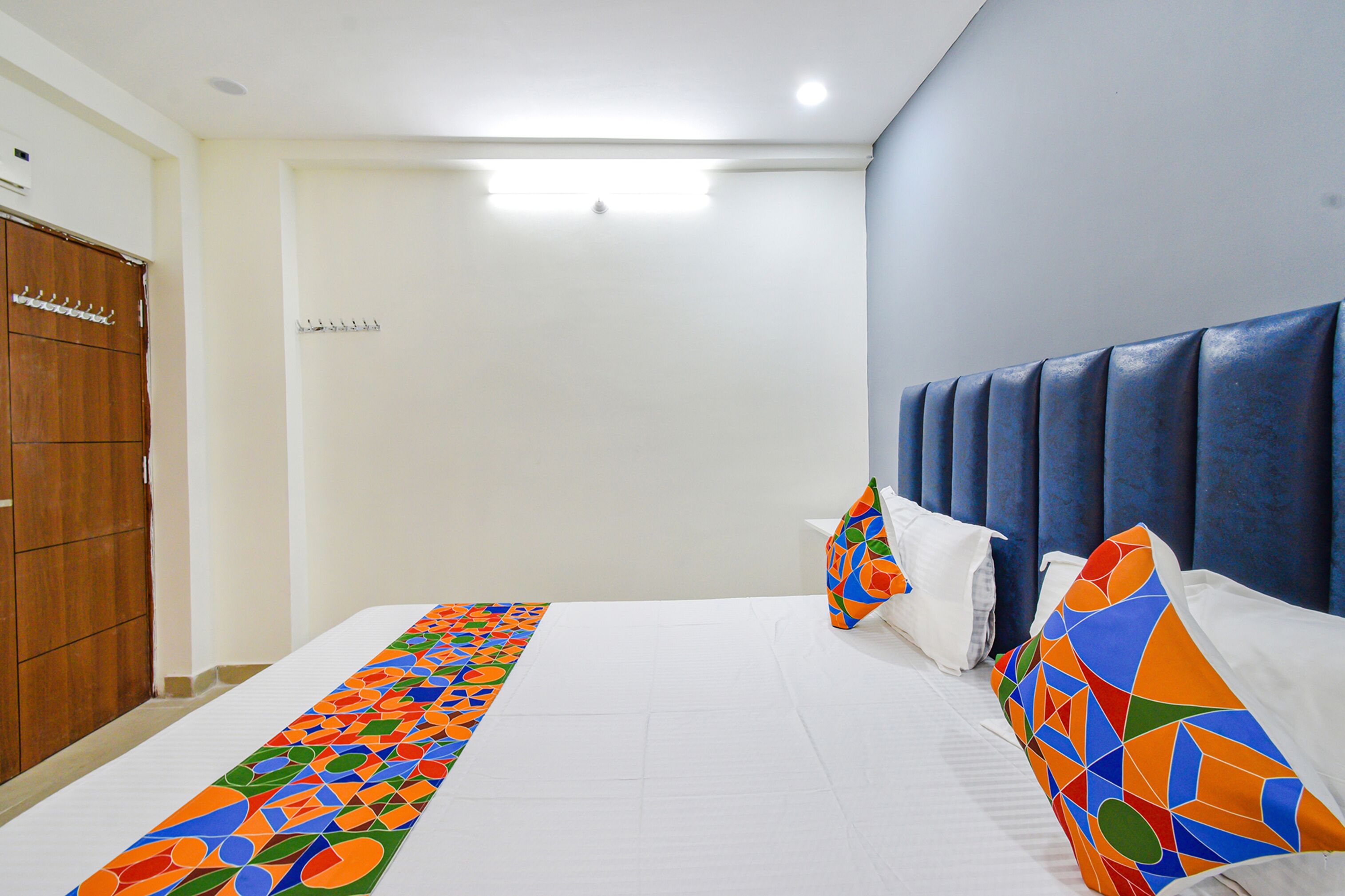 A hotel room with a large bed, a wooden wardrobe, and a blue headboard.