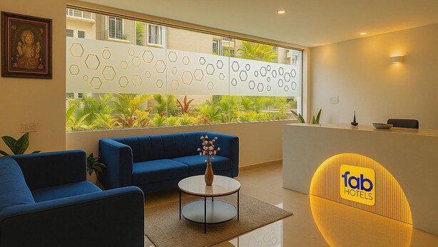 A hotel reception area with a blue sofa, a round table with a vase, and a reception desk with a logo. - Fabhotel Maski Suites (Hyderabad)