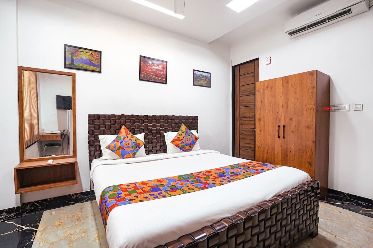Habitación de hotel con una cama grande, un armario de madera, un espejo y dos cuadros en la pared.