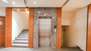 An elevator with a digital display, a carpeted floor, and a staircase with wooden panels. - FabHotel Prime The Vintage Inn - Hosur Road (Bengaluru)