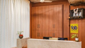 A reception desk with a sign reading "RECEPTION," wooden cabinets, a ceiling fan, and potted plants. - FabHotel Prime The Vintage Inn - Hosur Road (Bengaluru)