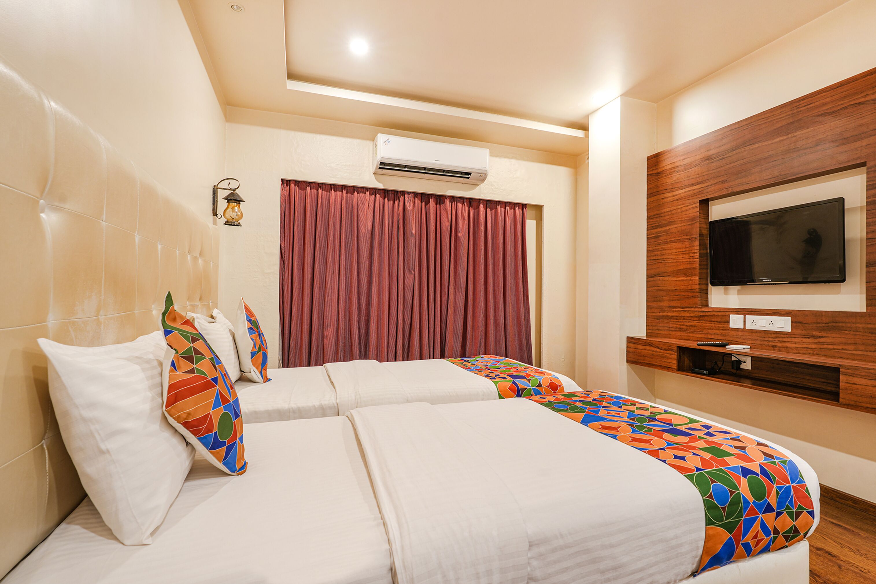 A hotel room with a large bed, a TV mounted on the wall, and an air conditioning unit above the bed.