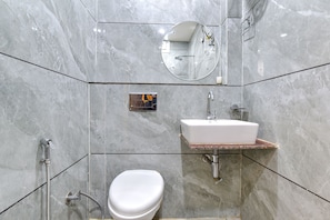 A modern bathroom with a marble wall, a white toilet, a sink with a marble countertop, and a shower with a handheld showerhead. - Fabhotel Heaven Palace (Haridwar)