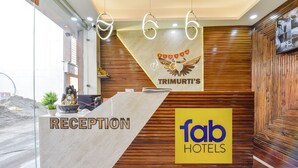 A reception area with a marble counter labeled "RECEPTION" and a "TRIMURTI'S" banner above. A "fab HOTELS" sign is also visible. - Fabhotel Heaven Palace (Haridwar)