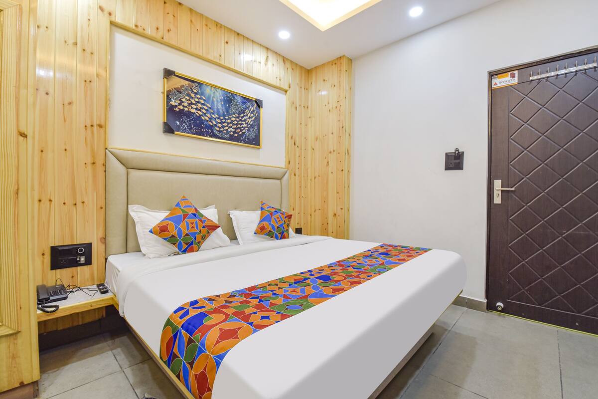 A bedroom with a bed, wooden panel walls, a painting, a door, and a bedside table with a phone.