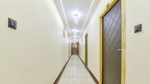 A long, narrow hallway with a shiny tiled floor, a wooden baseboard, and a door with a diamond-patterned glass panel on the right. - Fabhotel Heaven Palace (Haridwar)