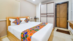 A neatly made bed with a colorful blanket, a wooden headboard, and a bedside table with a lamp. - Fabhotel Seri (Hyderabad)
