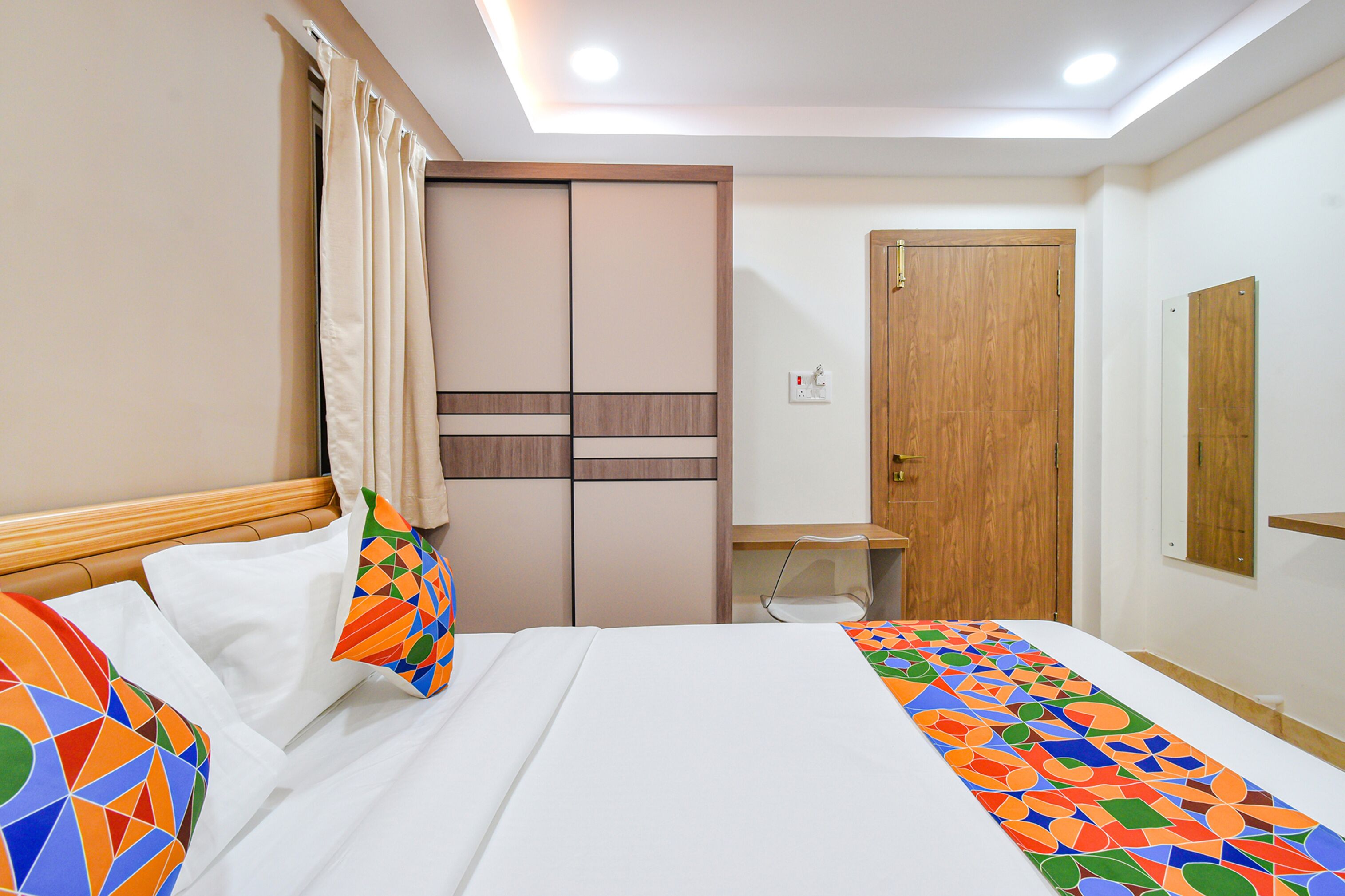 A hotel room with a bed, a desk, a wardrobe, and a mirror.