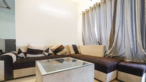 Un salon moderne avec un canapé d’angle, une table basse en verre et une grande fenêtre agrémentée de rideaux.