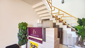 Un hall d’accueil moderne avec un escalier, des plantes en pot et un comptoir de réception où figurent le nom et le logo de l’hôtel.