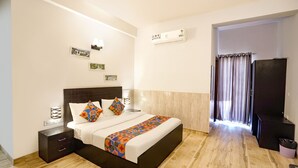 Une chambre bien rangée, avec un lit, des tables de chevet, un climatiseur fixé au mur et une vue sur l’extérieur, visible à travers une porte.