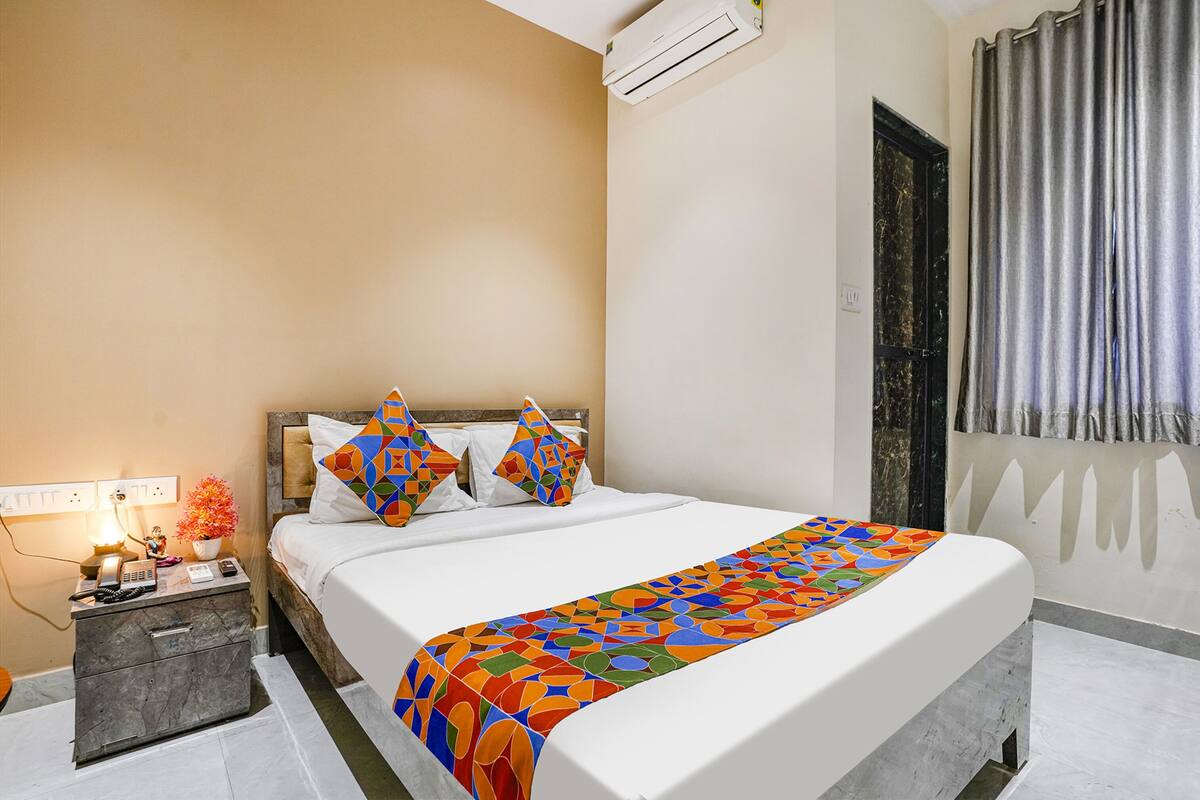 A hotel room with a bed, nightstand, and an air conditioning unit.