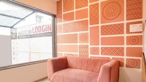 Un canapé rose dans une pièce dont le mur est orné d’un motif et qui possède une fenêtre sur laquelle est affiché un panneau indiquant « MAJESTIC INN LODGING ».