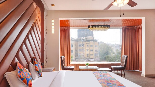 Une chambre d’hôtel dotée d’un grand lit, offrant une vue sur la ville, d’un ventilateur de plafond et d’un coin repas avec une table et des chaises.