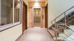 Un pasillo con una puerta de vidrio, una puerta de madera y una escalera con barandas de metal.