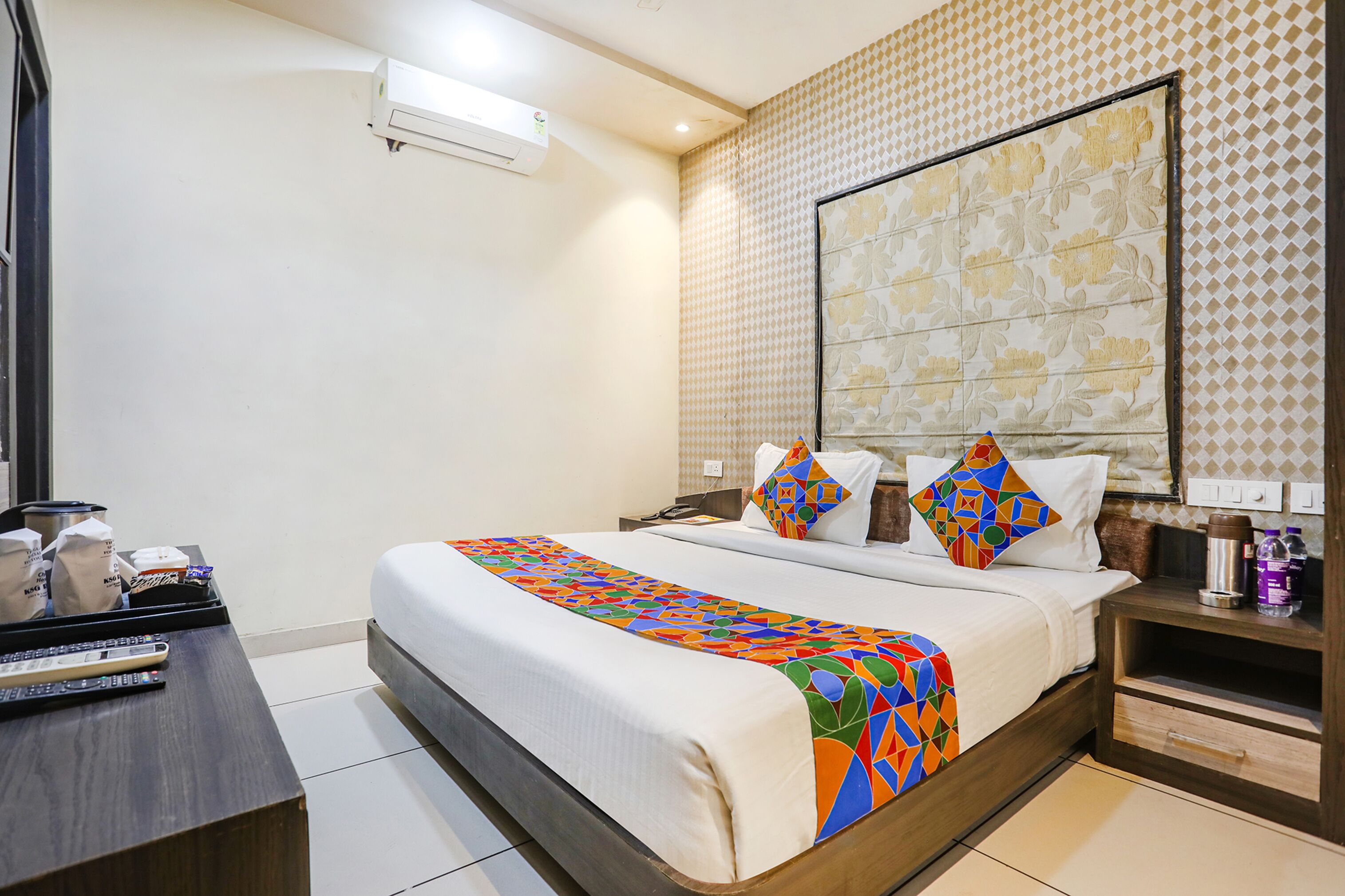 A hotel room with a large bed, a bedside table with a coffee maker, and a nightstand with a lamp.