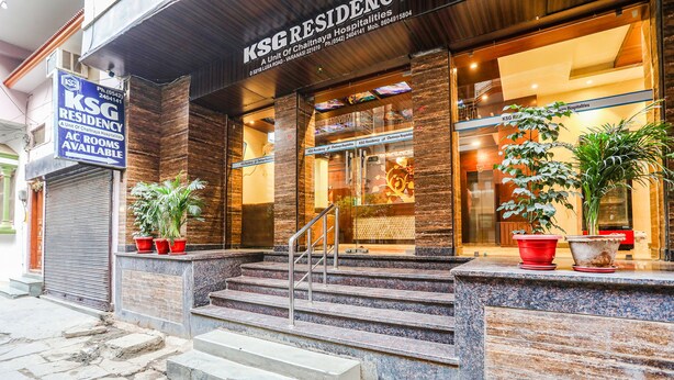 Entrada de un hotel con un cartel que dice KSG Residency, una escalera que conduce a la entrada y plantas en macetas en los escalones.
