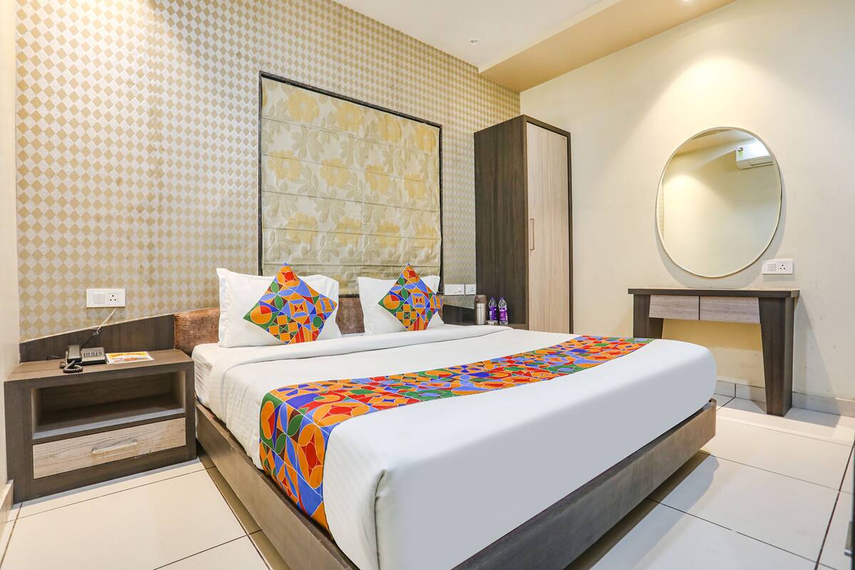 A hotel room with a large bed, a nightstand, a dresser, a mirror, and a patterned wall.