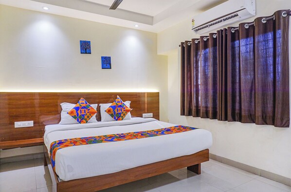 Habitación de hotel con una cama, cabecero, aire acondicionado de pared y ventana con cortinas.