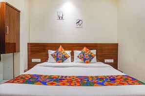 A hotel room with a wooden headboard, two pillows with colorful geometric patterns, a white bedspread, and two small artworks on the wall. - Fabhotel Phoenix Inn (Pune)
