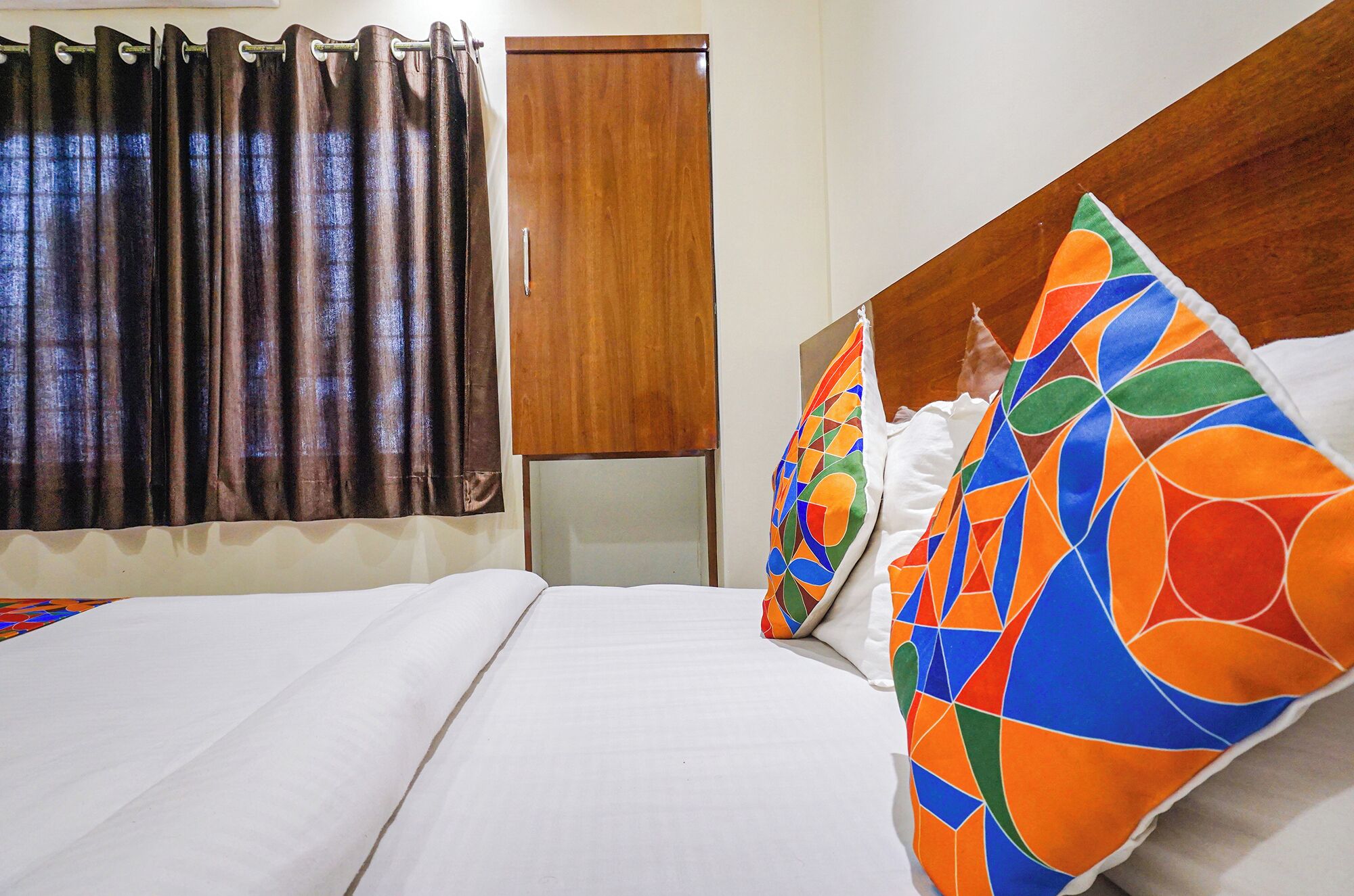 Habitació d'hotel amb un llit, cortines, un armari de fusta i un coixí de colors.