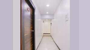 Un couloir étroit et bien éclairé, avec une porte en bois sur la gauche et une porte blanche au fond.