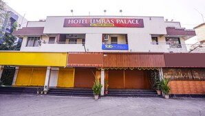 Un hôtel appelé Hotel Limras Palace, proposant des chambres climatisées et non climatisées, une façade avec des volets jaunes et bruns, et des plantes en pot à l’entrée.