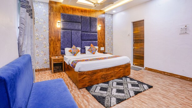 Une chambre avec une tête de lit en bois, un lit avec une literie blanche et des coussins colorés, un canapé bleu, un tapis à motifs et une porte en bois.