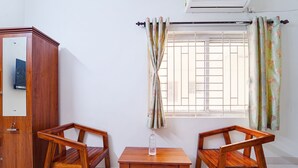 A room with a wooden cabinet, two wooden chairs, a small table, and a window with curtains. - Fabhotel Crosscut (Coimbatore)