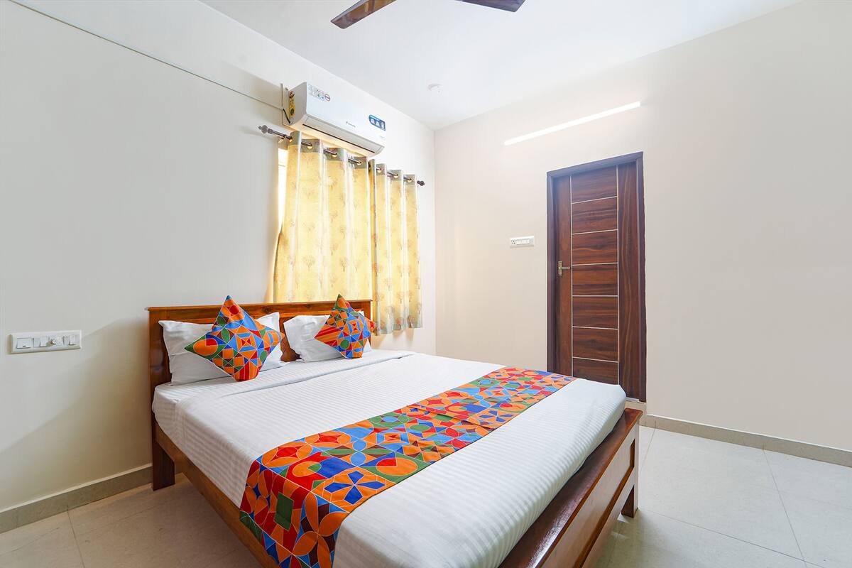 A neatly made bed with a colorful geometric-patterned blanket, a wooden headboard, and a wall-mounted air conditioner.