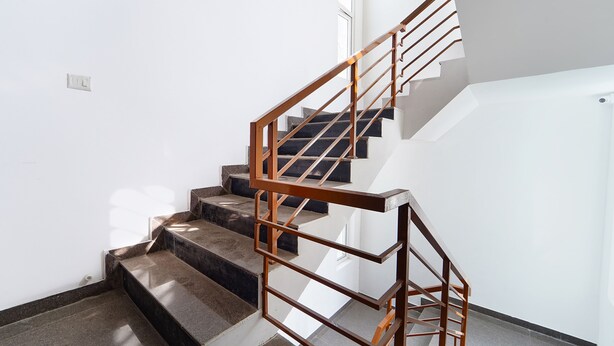 A staircase with a wooden handrail and black steps, leading to a landing with a white wall and a window. - Fabhotel Crosscut (Coimbatore)