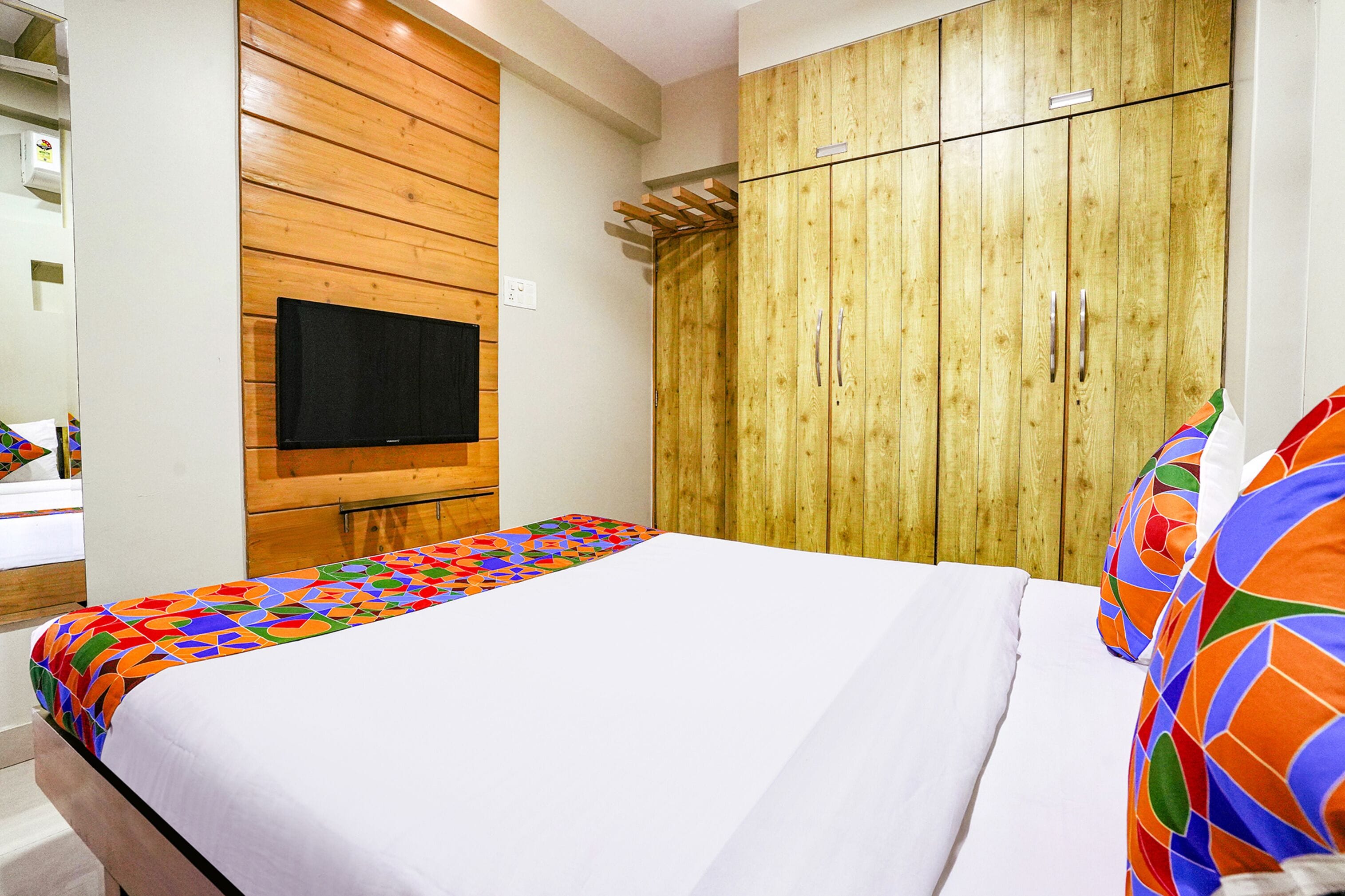 Una camera d'albergo con un letto, una TV a parete e un armadio in legno.