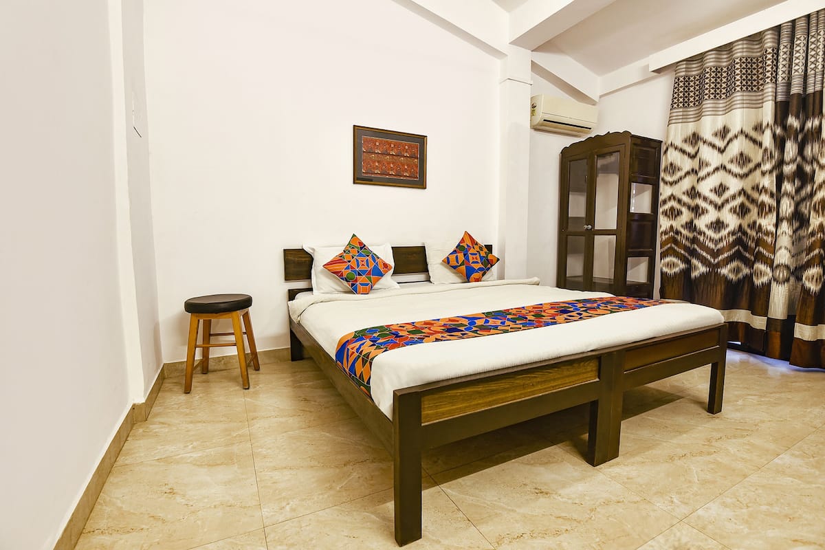 A bedroom with a wooden bed, a nightstand, a stool, a wardrobe, and a patterned curtain.