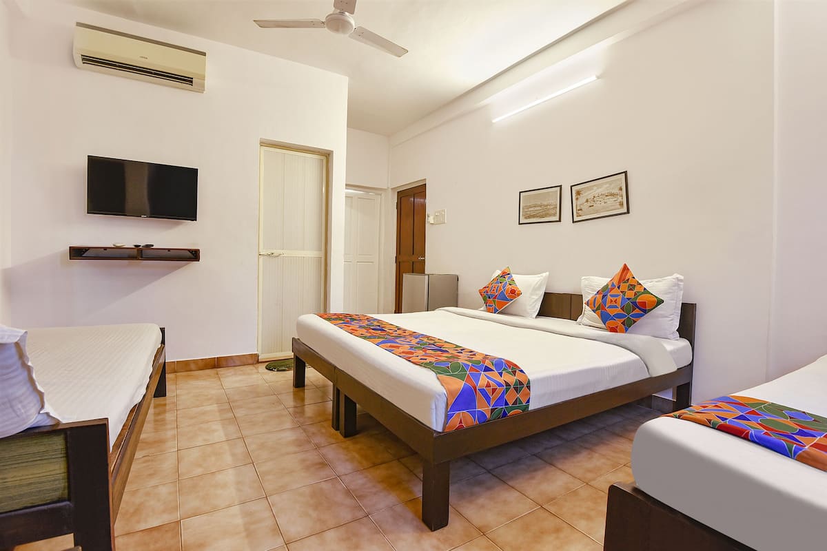 A hotel room with a bed, a TV, a ceiling fan, and a door.