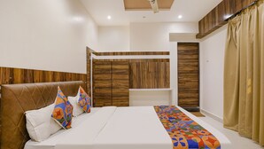 A hotel room with a large bed, a wooden wardrobe, a small table, and a ceiling fan. - Fabhotel Silver Cloud (Mumbai)