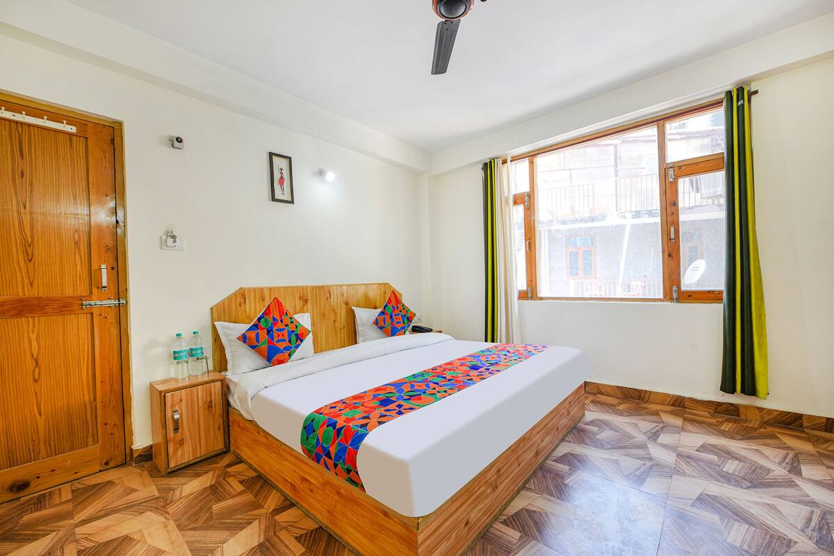 A bedroom with a wooden bed, a nightstand with water bottles, a wooden wardrobe, and a window with curtains.