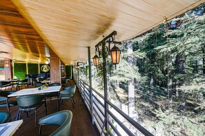 Un restaurante con techo de madera, mesas al aire libre y vistas a un bosque.