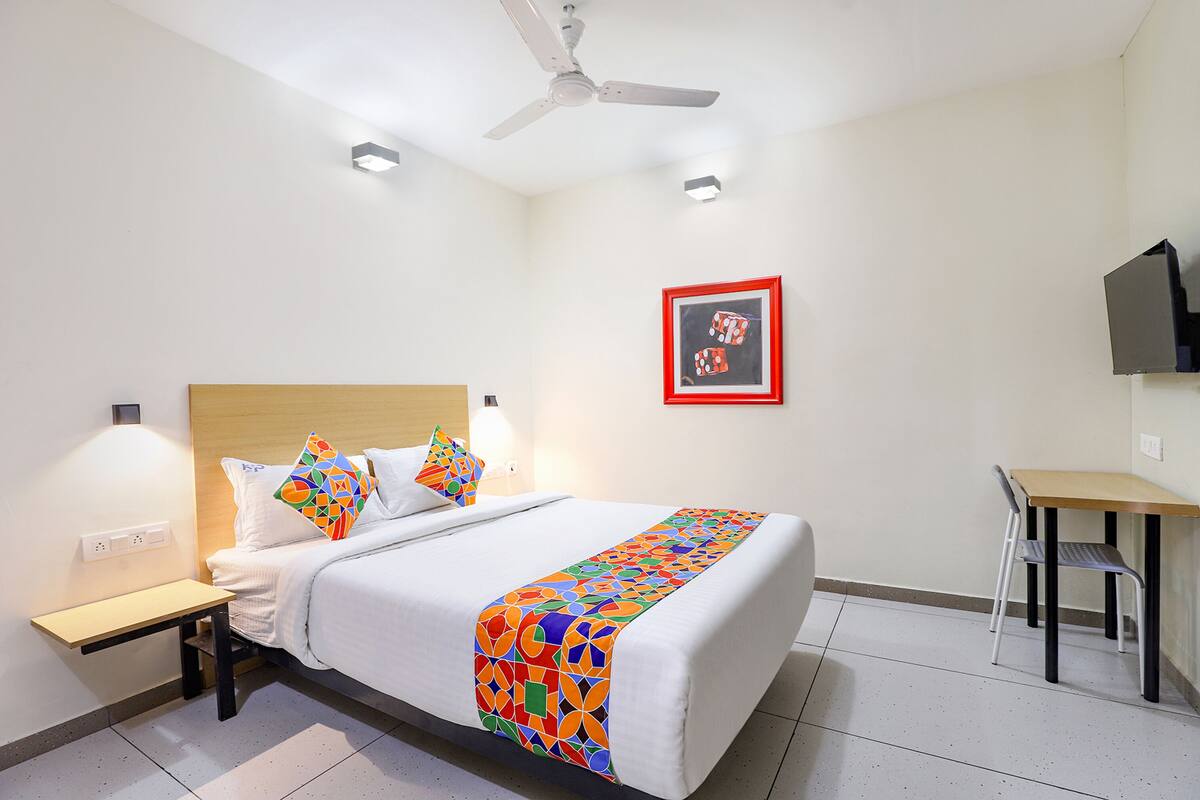 A hotel room with a bed, bedside table, chair, desk, and a ceiling fan.