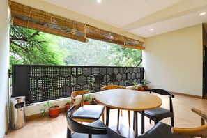 A dining area with a round table, black chairs, potted plants, and a view of greenery through a bamboo blind. - Fabhotel Kp (Chennai)