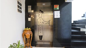 An elevator with a person holding a phone, a sign indicating maximum 3 persons, and a sign instructing to use the stairs in case of fire. - Fabhotel Kp (Chennai)