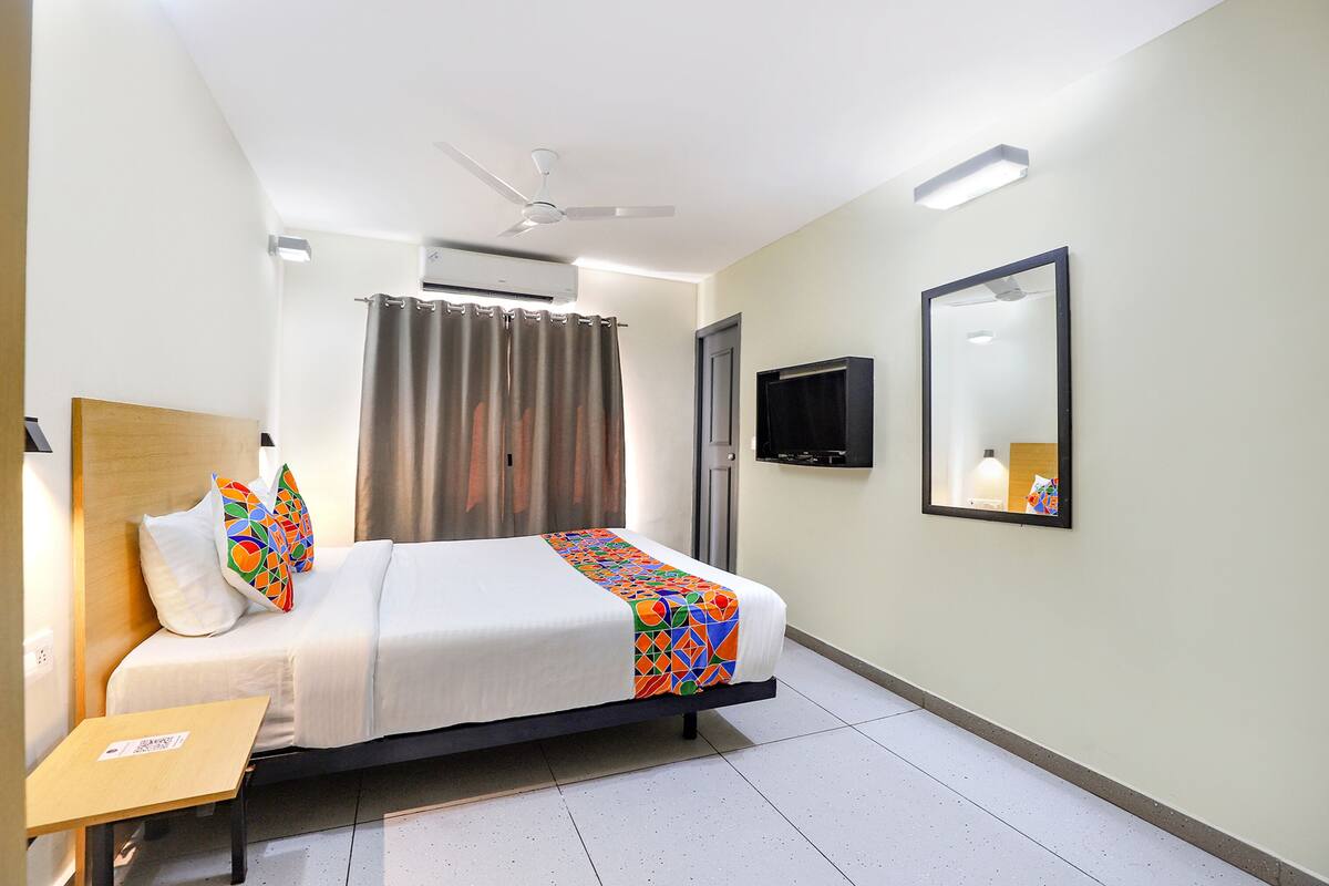 A hotel room with a bed, a TV, a ceiling fan, and an air conditioning unit.
