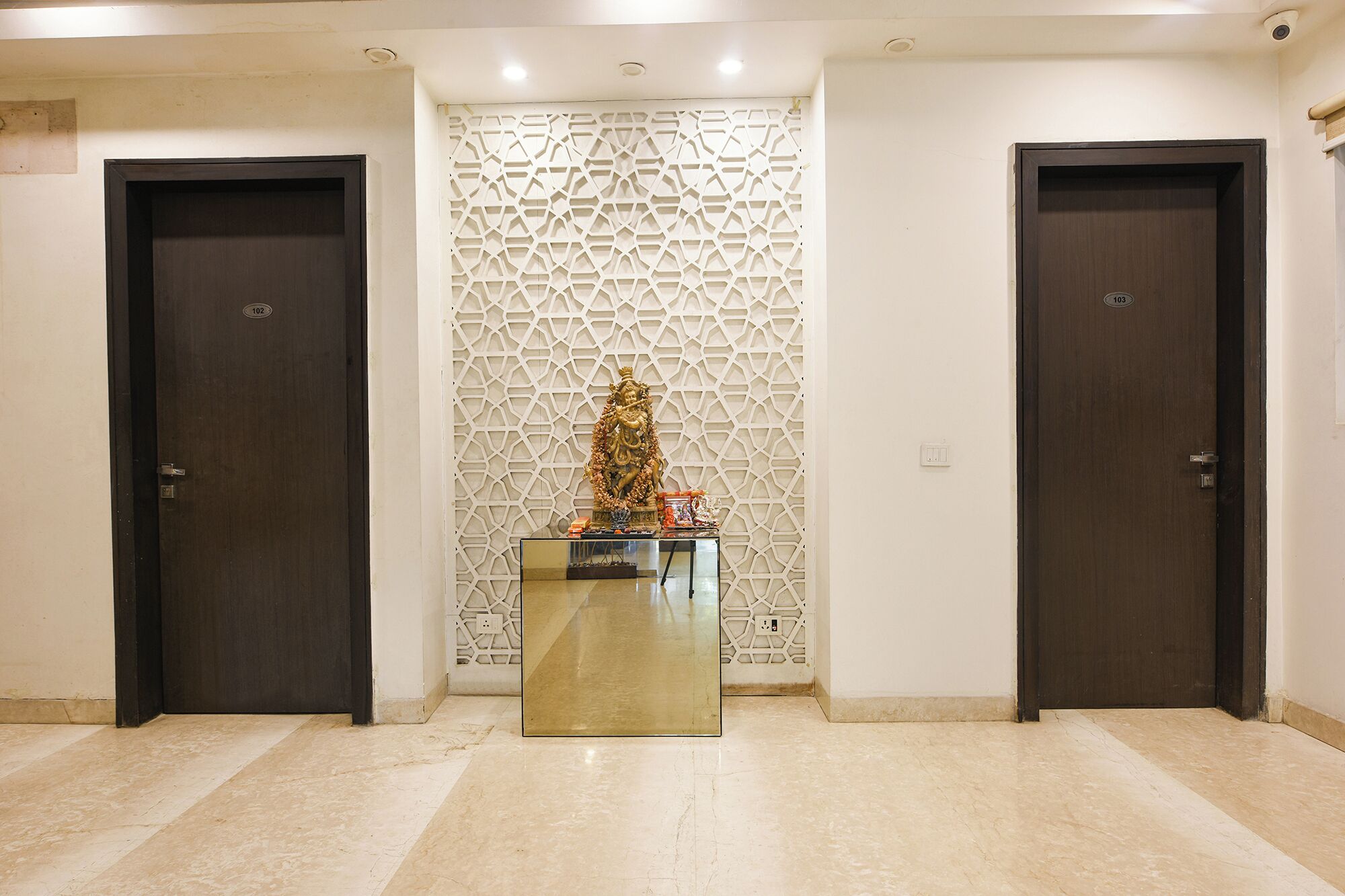 A hallway with two dark wooden doors, a decorative wall with a geometric pattern, and a small altar with religious items.