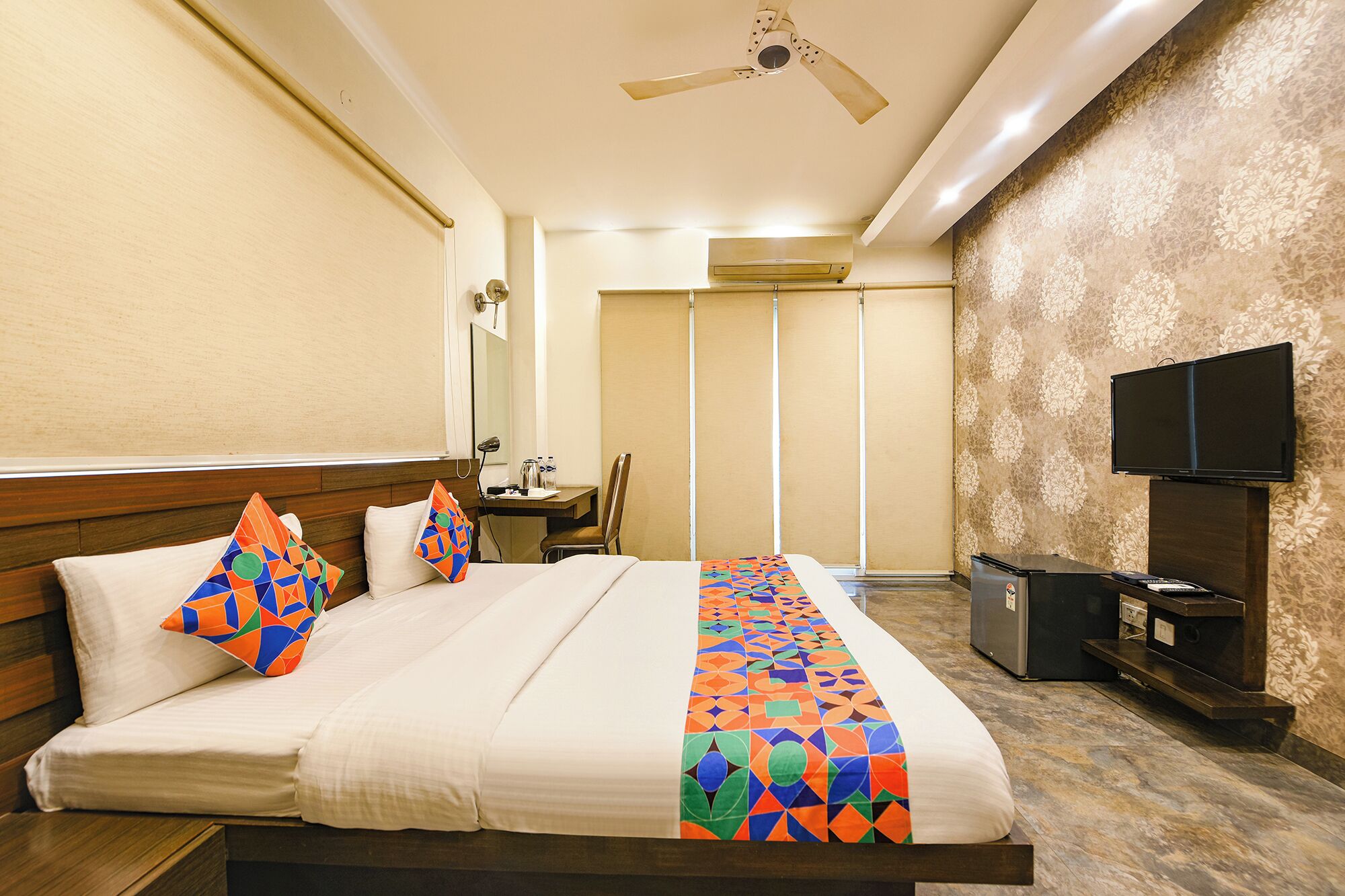 A hotel room with a bed, a desk, a chair, a television, and a ceiling fan.