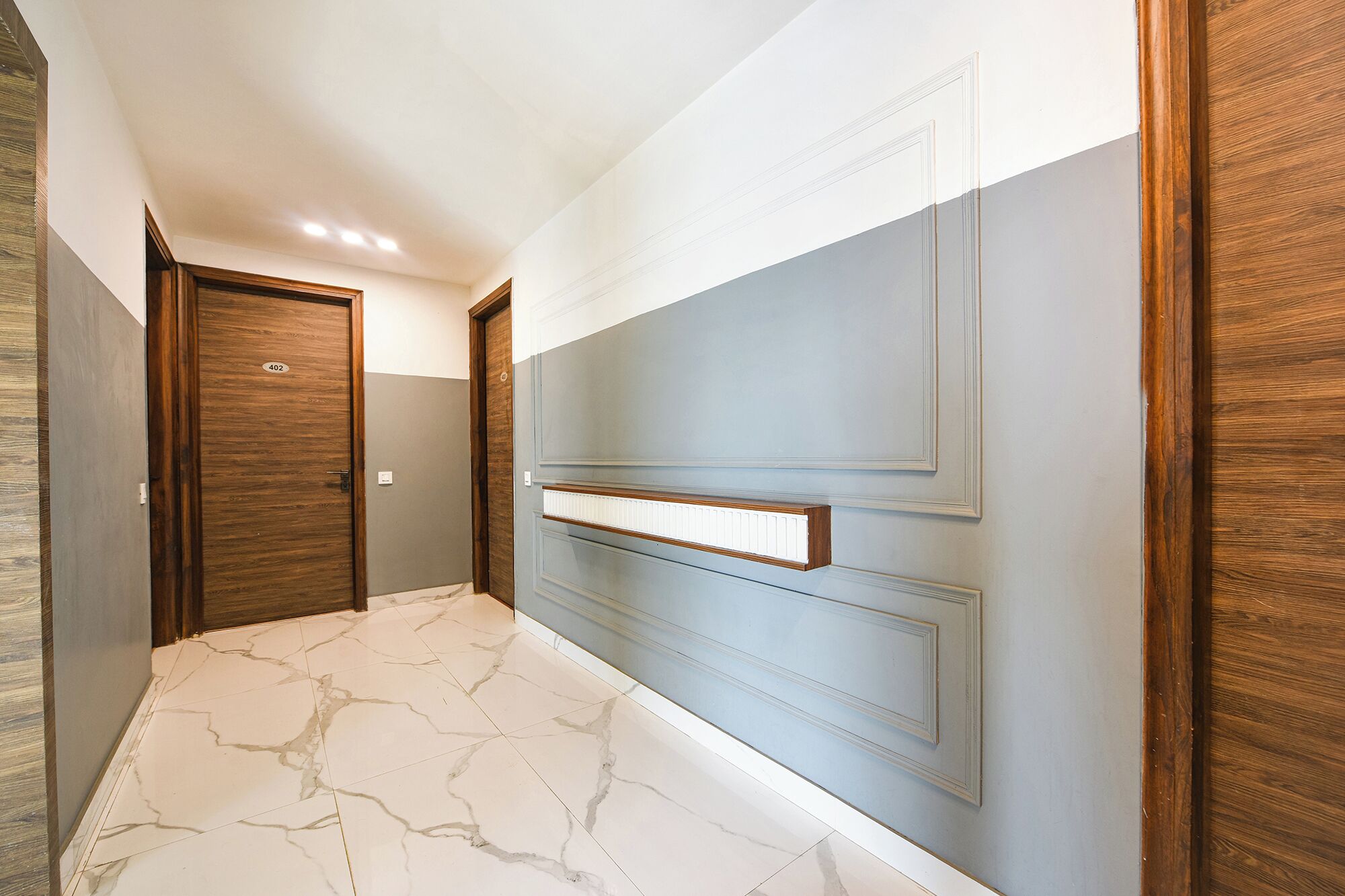 A hallway with marble flooring, wooden doors, and a light blue wall with a recessed shelf.