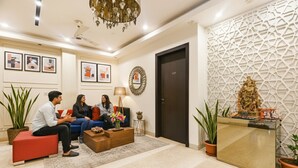 A modern reception area with a reception desk, a chandelier, framed artwork on the walls, and potted plants. - Fabhotel Micasa (Gurugram)