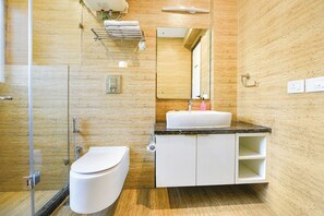 A modern bathroom with a glass shower enclosure, a white toilet, a sink with a black countertop, and a mirror above the sink. - Fabhotel Micasa (Gurugram)
