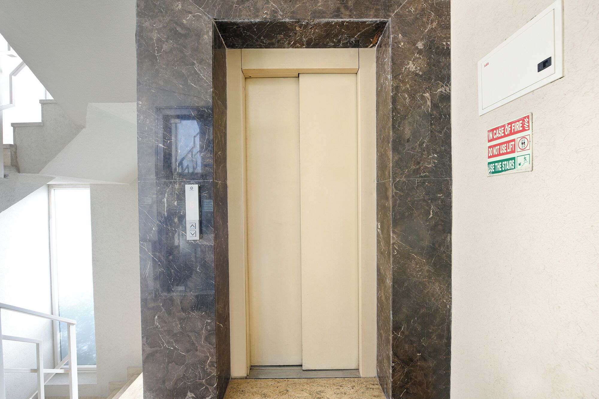 An elevator with a marble wall, a fire safety sign, and a door with a control panel.