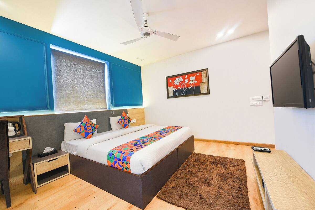 A modern bedroom with a bed, a desk, a chair, a TV, and a ceiling fan.
