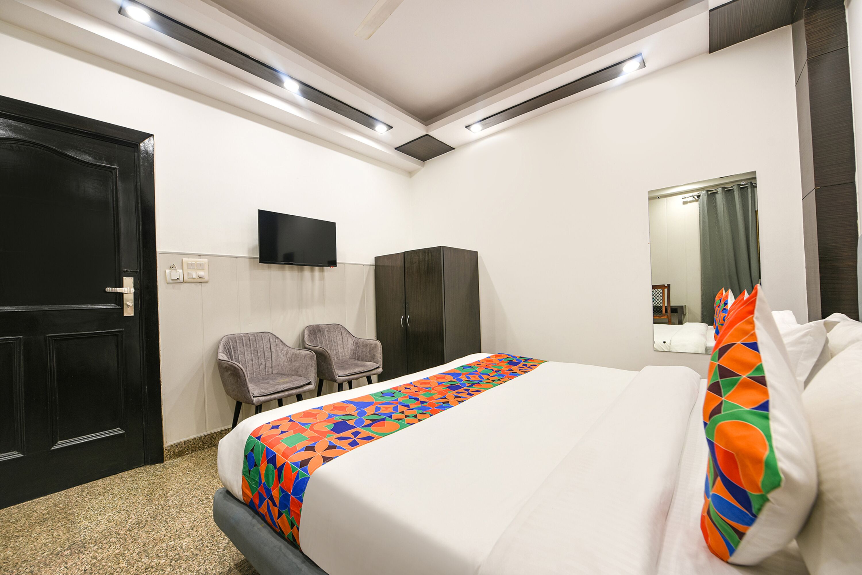 Habitación de hotel con cama, televisor montado en la pared, armario y dos sillas.