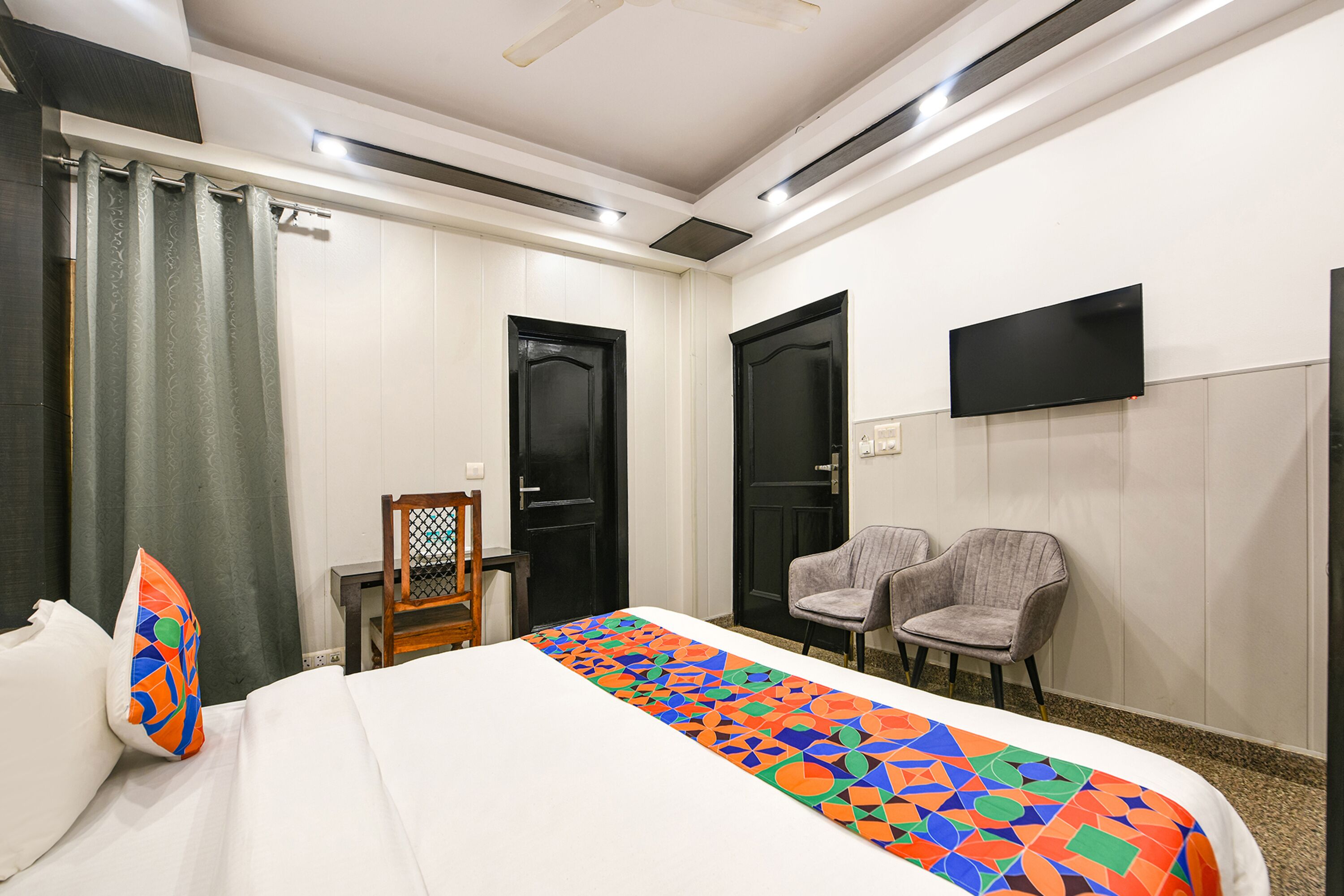 A hotel room with a bed, two chairs, a TV, and two doors.